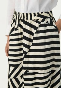 Jupe rayée noire et blanche en tissu texturé. Taille élastique, arborant un mélange de rayures horizontales et de motifs angulaires.