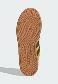 Semelle de basket en caoutchouc avec motif d'adhérence texturé. Dispose d'une base jaune avec des rayures noires et un logo en relief.