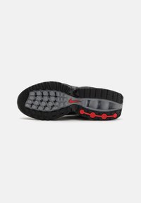Semelle de chaussure Nike noire avec motif en caoutchouc texturé et accents circulaires rouges. Sections translucides révélant des éléments amortissants. Forme arrondie.
