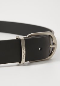 Cintura in pelle nera con fibbia in metallo argentato. La fibbia presenta una finitura lucida e include il logo "Calvin Klein".