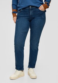 Vaqueros de mezclilla azul oscuro con un corte clásico, cinco bolsillos, detalles de costura sutil, combinados con zapatillas blancas.