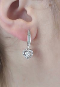 Zilveren drop oorbellen met een hartvormige hanger waarin een grote heldere steen is verwerkt, omringd door kleinere stenen, die hangt aan een gestructureerde lever-back haak.
