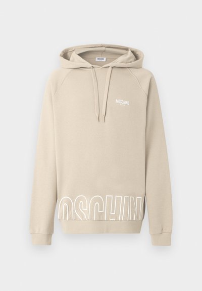 Sweat à capuche Moschino beige avec cordons, petit logo sur la poitrine et grandes lettres blanches partiellement visibles près de l'ourlet inférieur.