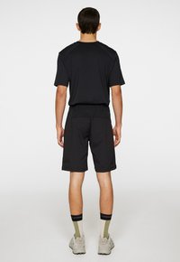 Svart kortärmad skjorta och svarta shorts, båda i ett lätt tyg. Synlig elastisk midja och neutrala strumpor med accenter.