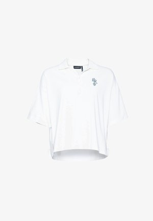 Valkoinen ylisuuri lyhythihainen poolopaita, jossa on kaulus, nappilista, sivuhalkiot ja pieni sininen kuvio vasemmassa rinnassa.