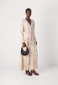 Pitkä beige mekko, jossa on geometrisellä valkoisella kuviolla, napit edessä ja nauhavyötärö. Yhdistetty mustan kaarevan käsilaukun ja remmistöisten mustien mokkasiinien kanssa.