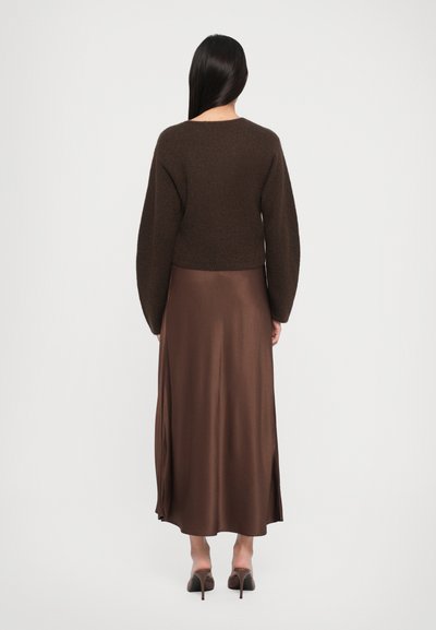 Brown cropped sweater with textured knit and long sleeves paired with a satin brown maxi skirt featuring a side slit. Heeled shoes complete the look.