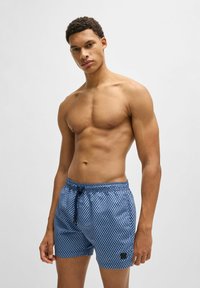 Blue patterned swim shorts with an elastic waistband and drawstring, featuring a small black logo patch on the left leg.