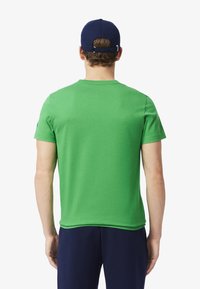 Vihreä puuvillapaita, jossa on lyhyet hihat ja pyöreä kaula-aukko. Tummansininen hattu päässä, jossa on kangasremmi ja valkoista ommeltua yksityiskohtaa.