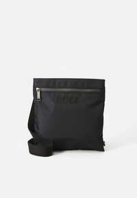 Črna najlonska torbica čez ramo z nastavljivim trakom, z zadrgo na žepu in vbočenim napisom "BOSS" na sprednji strani. Površina z teksturo.