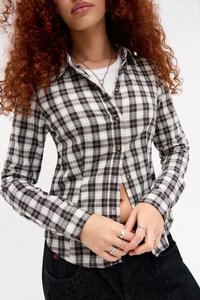 Camicia a quadri in bianco, nero e beige. Maniche lunghe, chiusura con bottoni, colletto e tessuti con una texture liscia. Dettagliata con bottoni.