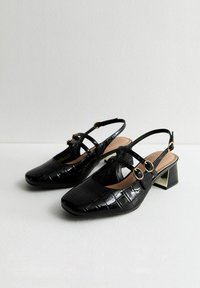 Svarta patenterade skinnslingback-skor med kvadratisk tå, med två remmar med guldfärgade detaljer och en låg klack. Textur med krokodilprägling.