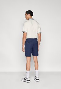 Ανοιχτόχρωμο πόλο πουκάμισο με γκρι γιακά, συνδυασμένο με ναυτικού χρώματος κοντό παντελόνι. Η εμφάνιση έχει κομψό σχεδιασμό, με τσέπες και διακριτικές λεπτομέρειες.