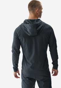 Sudadera deportiva de un gris oscuro con un acabado texturizado, que cuenta con una capucha ajustable con cordón y puños acanalados. Diseño ajustado.
