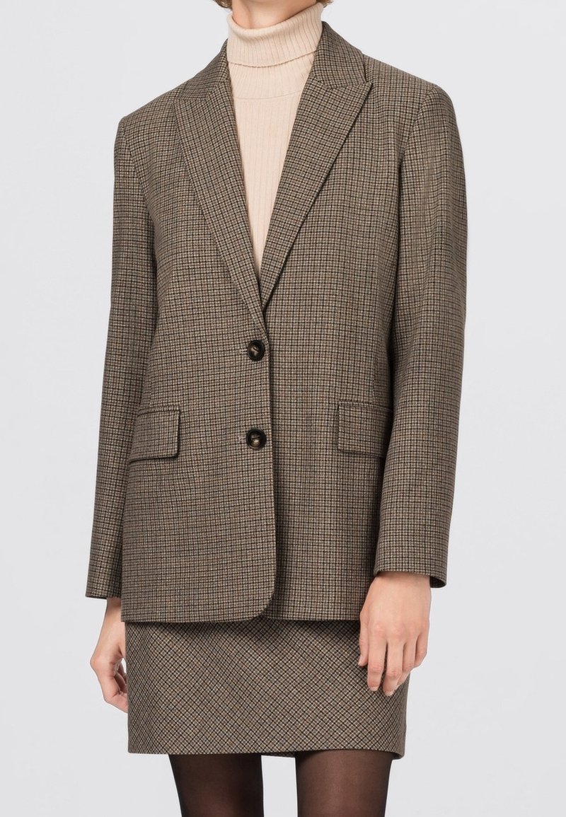 Veste blazer marron à carreaux avec revers crantés, deux boutons et poches avant, portée sur un col roulé beige clair et une jupe assortie.