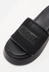 Black slide sandal featuring a textured mesh strap and a smooth sole. Prominent DKNY logo embossed on the strap. Minimalistic design.