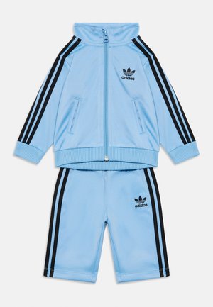 Lys blå polyester treningsdrakt med svarte tre-stripes aksenter, glidelåsjakke, to frontlommer og brodert svart logo på begge deler.