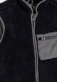 Gilet senza maniche blu navy con corpo in pile testurizzato, dettagli in tessuto grigio, tasca frontale con zip e chiusura a zip completa sul davanti.