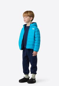 Μπλε μπουφάν puffer με κουκούλα και λογότυπο, ναυτικά παντελόνια φόρμας, στρωμένες πράσινες και εκρού καρό κάλτσες και μαύρα παπούτσια τύπου slip-on.