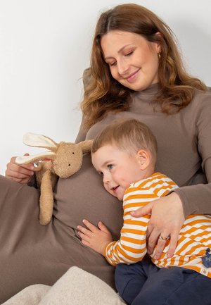 Abito a coste marrone indossato da una donna con un giocattolo a forma di coniglio di peluche, un bambino in una maglietta a righe arancione e bianca si stringe contro il suo pancione.