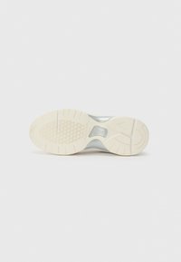 White sneaker sole with a textured rubber bottom, featuring a smooth silver upper and a logo on the midsole. Hexagonal pattern for grip.