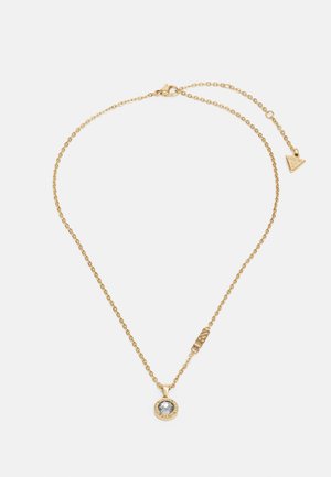 Colar de corrente dourada com um pendente redondo com uma pedra central, detalhes texturizados e uma pequena etiqueta da marca na corrente.