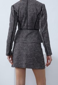 Tailored jacket dress in textured black and white fabric, featuring contrasting black piping and structured shoulders. Short length and fitted silhouette.