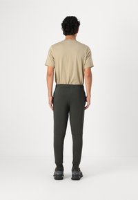 Beige kortærmet skjorte med rund hals, kombineret med mørkegrønne tapered joggerbukser. Bukserne har en elastisk talje og manchetter ved anklerne.