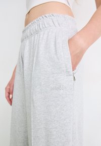 Lichtgrijze joggers met elastische tailleband en zijzakken. Kenmerken zijn het gestikte logo op het been en de geribbelde tailleband. Zachte katoenen stof met een gladde textuur.