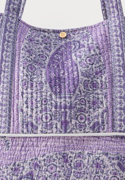 Sac en tissu matelassé violet et blanc avec des motifs floraux et de feuilles, doté de sangles et d'une petite fermeture à bouton en bois rond.
