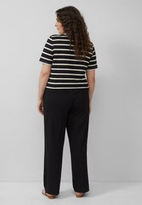 Gestreepte top met korte mouwen in zwart en crèmel, gecombineerd met losse zwarte broeken. De stof lijkt zacht, met een relaxte pasvorm en minimale details.