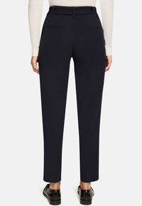 Pantalon bleu marine coupé sur mesure avec une texture lisse, doté d'une taille haute et de deux poches arrière, assorti à des chaussures noires.