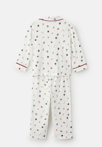 Beli pižami z dolgimi rokavi in rdečimi detajli, ki vsebujejo praznične motive, kot so moški iz ingverjevega kruha, bonboni, holly in cvetlični elementi.