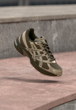 Running shoe with mesh and synthetic upper in olive green and tan, featuring padded collar, laces, and visible cushioning in sole.