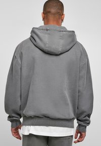 Felpa grigia oversized con cappuccio regolabile, polsini e fascia in vita a coste. Tessuto morbido e texturizzato con una vestibilità comoda.