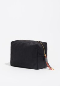 Neceser negro con forma geométrica. Presenta un zipper dorado, tejido texturizado y un acento de borlas coloridas en la tira del zipper.