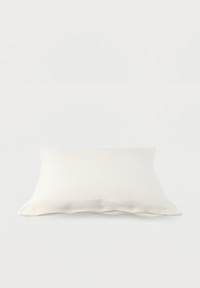 Λευκό ορθογώνιο μαξιλάρι με λεπτομέρειες κουμπιών στο άκρο, πάνω σε απλό ανοιχτόχρωμο φόντο.
