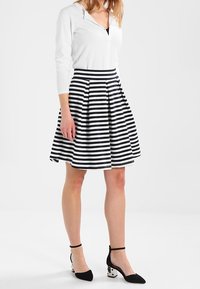 Gonna a righe bianche e nere con un design a campana, abbinata a una maglietta bianca a maniche lunghe e tacchi neri a punta con cinturini alla caviglia.