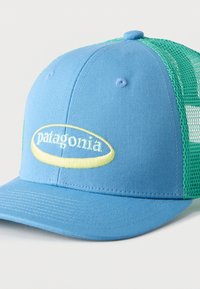 Μπλε και πράσινο δίχτυ αθλητικό καπέλο με κίτρινο οβάλ λογότυπο και κεντημένο κείμενο "Patagonia" στο μπροστινό πάνελ.