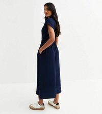 Mörkblå maxiklänning med korta �ärmar, elastisk midja, sidofickor och en slät textur, tillsammans med vita och beige sneakers.