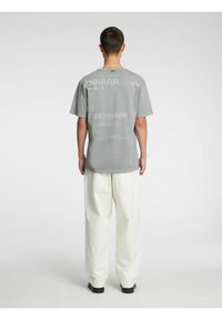 Grå bomulls-T-skjorte med trykt tekst og grafikk på ryggen, korte ermer, ledig passform, brukt sammen med hvite vidbukser.