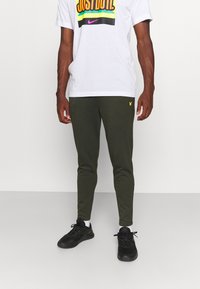 Groene joggebroek gemaakt van zachte stof, slim fit ontwerp, met een klein geel logo aan de zijkant. Gecombineerd met een wit T-shirt met grafische print.