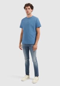 Blauwe katoenen t-shirt met korte mouwen, ronde halslijn en een klein tekstlogo op de borst. Gekocht met lichtblauwe denim en witte sneakers.