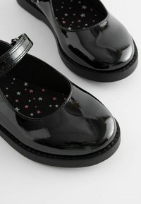 Zapatos Mary Jane de charol negro con punta redondeada, que presentan una correa y forro de tela con patrón de estrellas en rosa, plateado y blanco.