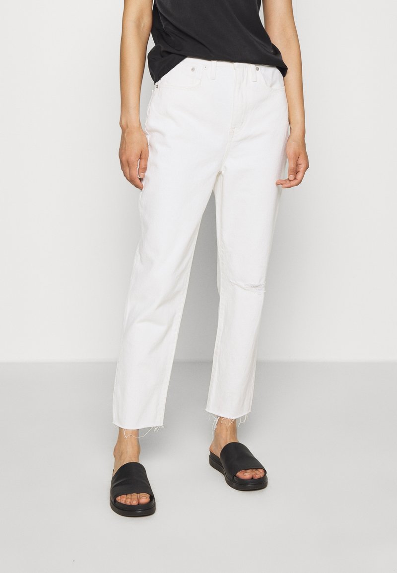 Valkoiset suorat farkut, joissa on risat lahkeet, yhdistetty mustaan lyhythihaiseen paitaan ja mustiin liukuvilla sandaaleihin, korostaa rentoa istuvuutta.