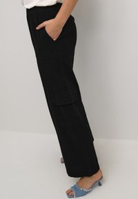 Zwarte cargobroek met een elastische tailleband en zijzakken, met een losse pasvorm en rechte pijpen. De stof heeft een matte textuur.