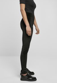 Svarte tights laget av mykt og elastisk stoff. Designet har høy midje og smal passform, i kombinasjon med glinsende svarte sko.