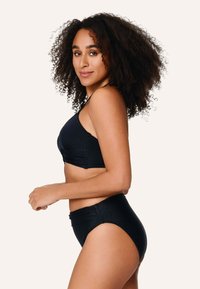 Musta bikinit-setti, joka sisältää tekstuurilla varustetun bralette-topin leveillä olkaimilla sekä korkea vyötäröiset alaosat, joissa on hienovaraisia rypytys yksityiskohtia.