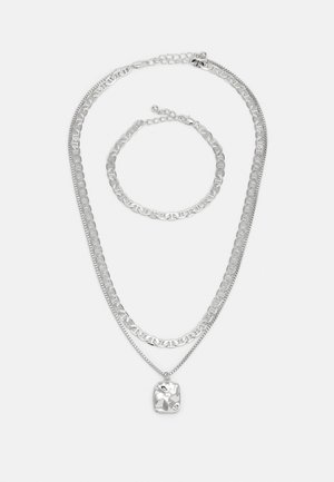 Silver multi-layered necklace and bracelet set featuring textured chains and a pendant with a smooth, reflective surface.