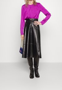 Fuchsia blus med lång ärm och plisseringar, ihop med en svart läderkjol i medellängd. Svarta knähöga stövlar och en liten blå handväska med kedjehandtag.